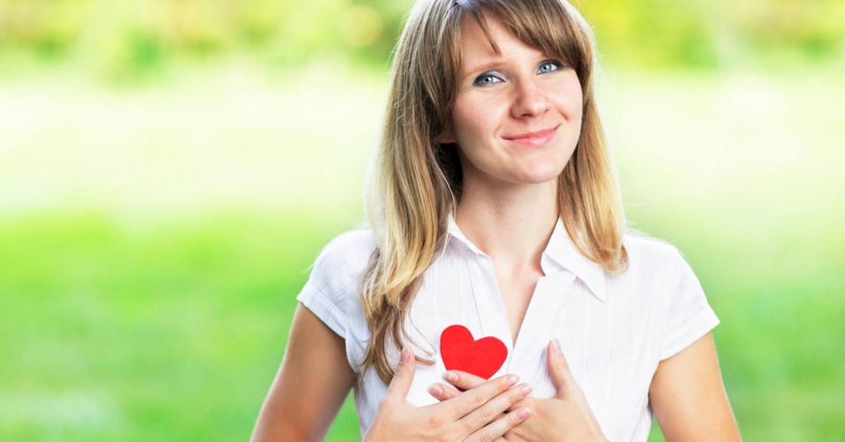 Young woman in love standing on nature holding a red paper heart